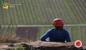 Man sieht win weiteres "Foto des Monats", eingereicht von Volkard Schwarz, "Weinbergblick". Eine junge Frau sitzt in den Felsengärten von Hessigheim und beobachtet die Landschaft.
