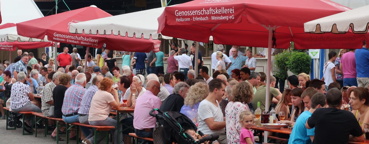 Menschen sitzen draußen an Tischen beim Heilbronner Sommerfest vor der Genossenschaftskellerei Heilbronn