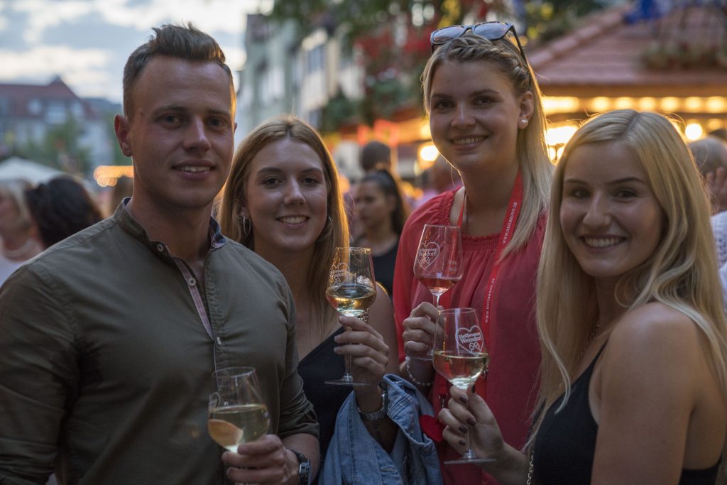 Vier junge Leute stehen am Abend auf dem Heilbronner Weindorf und halten Weißwein in der Hand. Eines der größten Events Württembergs im Zusammenhang mit Wein.