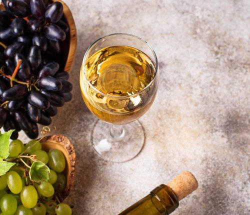 Irrtümer über Wein. Man sieht ein Glas Weißwein mit Trauben und einer Korkflasche