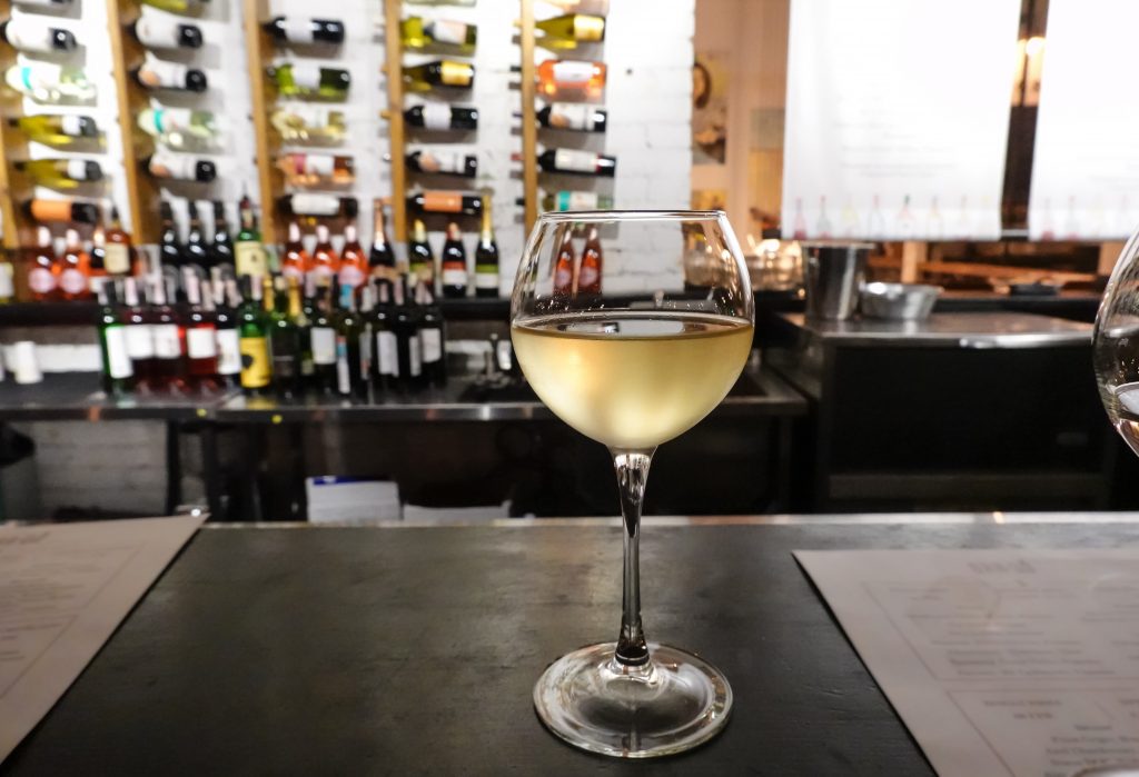 Weißwein im Glas vor einem Weinregal