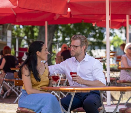 Ein Paar sitzt im Weinpavillon an der Neckarbühne unter einem Sonnenschirm und genießt ein Glas Wein