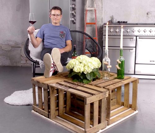 Weinkisten-Tisch DIY, man sieht einen Mann mit Weinglas auf einem Stuhl sitzen. Die Beine auf einen selbstgebauten Weinkisten Tisch gelegt