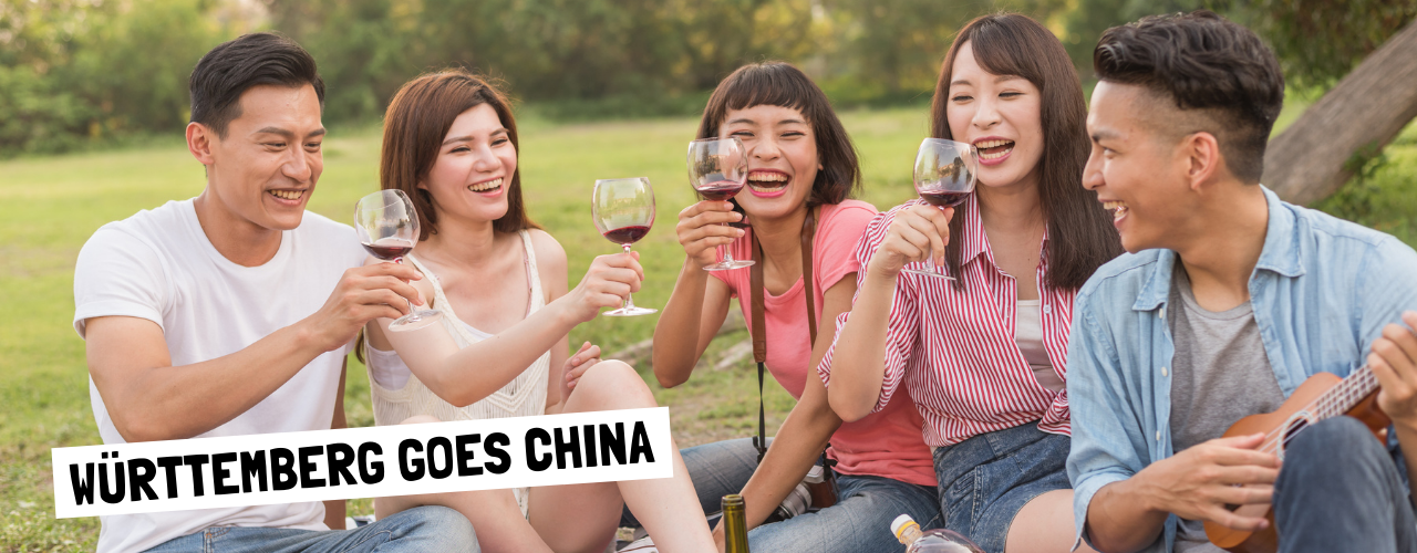 Junge Asiatinnen und Asiaten sitzen im Park, trinken Rotwein und lachen