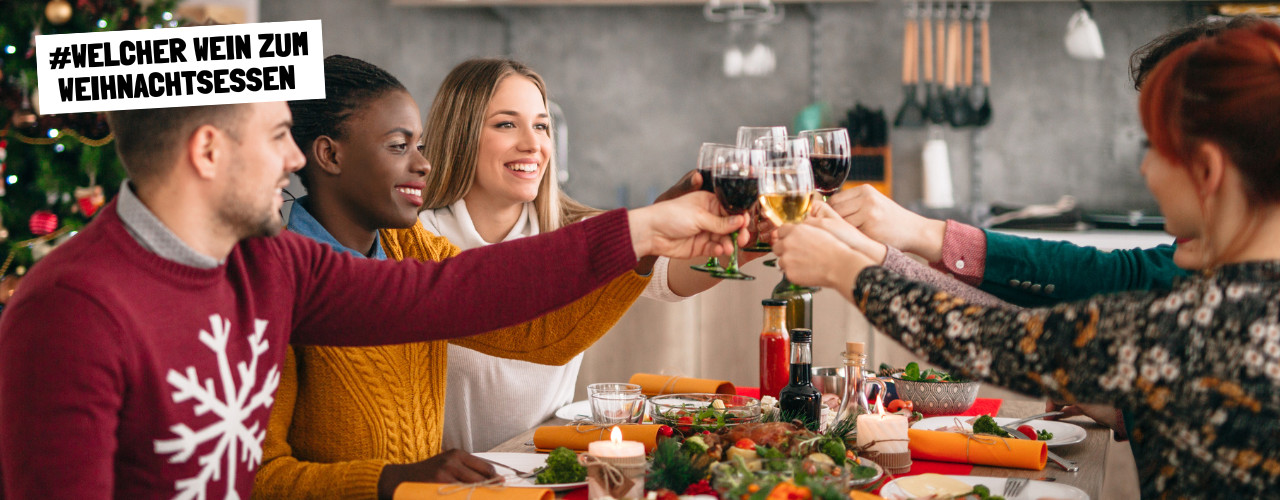 Junge Frauen sitzen am Weihnachtstisch beim Weihnachtsessen und stoßen mit Wein an