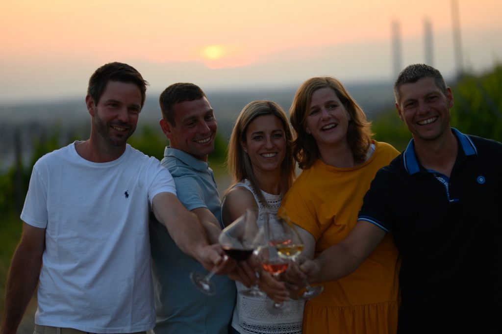 Mehrere junge Menschen stoßen im Sonnenuntergang mit Wein an