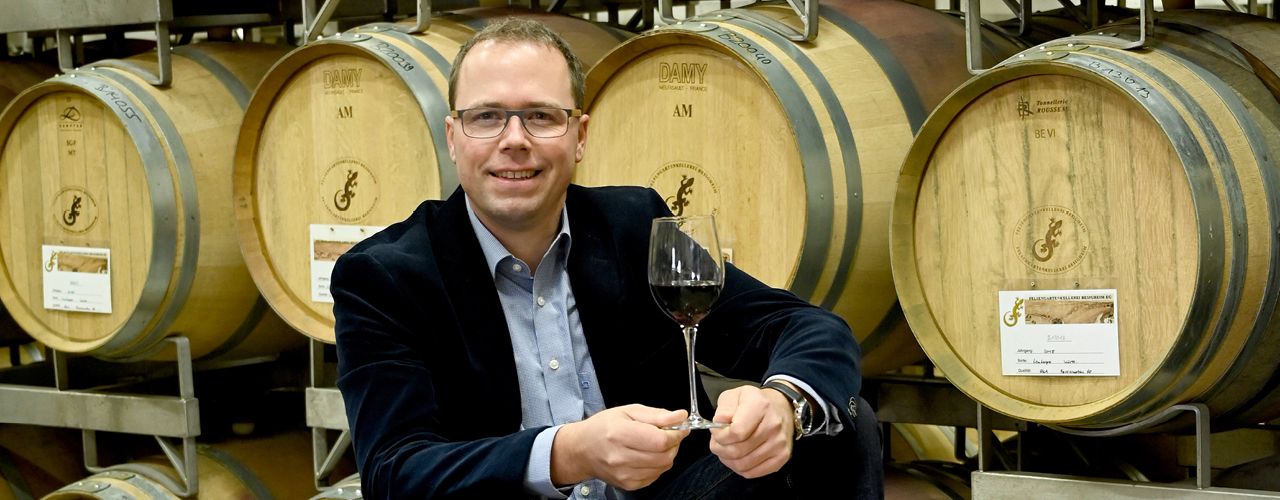 Sebastian Häußer, Oenologe und Betriebsleiter der Felsengartenkellerei Besigheim, sitzt im Holzfasskeller mit einem Glas Rotwein auf einem Fass