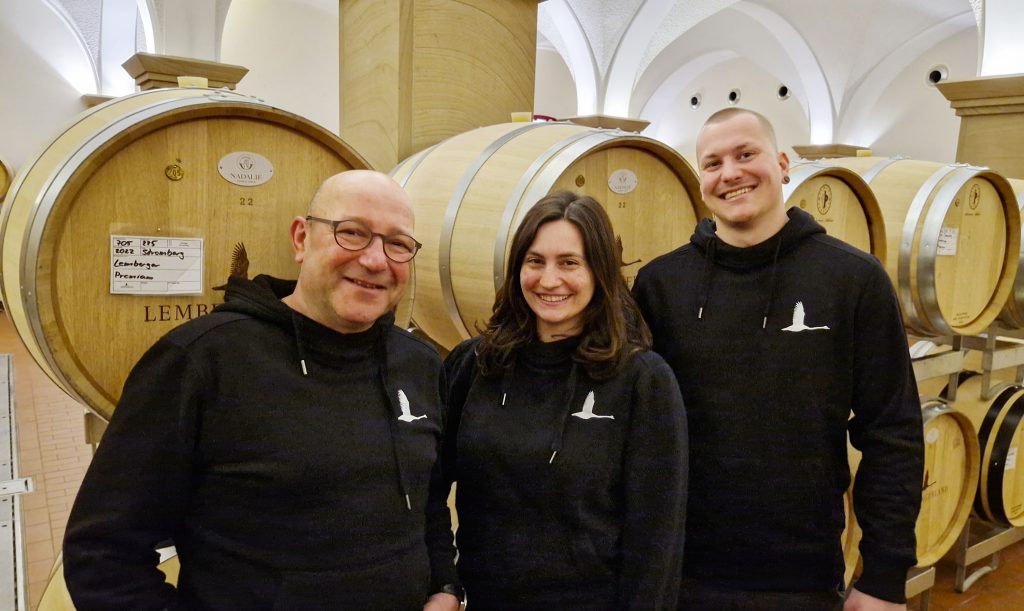 Thomas Hagenbucher, Lisa Ernst und Andreas Buchele stehen vor Weinfässern im Keller der Lembergerland Kellerei Rosswag