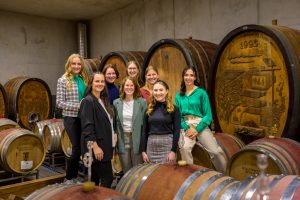 Die fünf Bewerberinnen um das Amt der Württemberger Weinkönigin 2023/24 sitzen zusammen mit den noch amtierenden Weinhoheiten im Weinkeller beieinander.