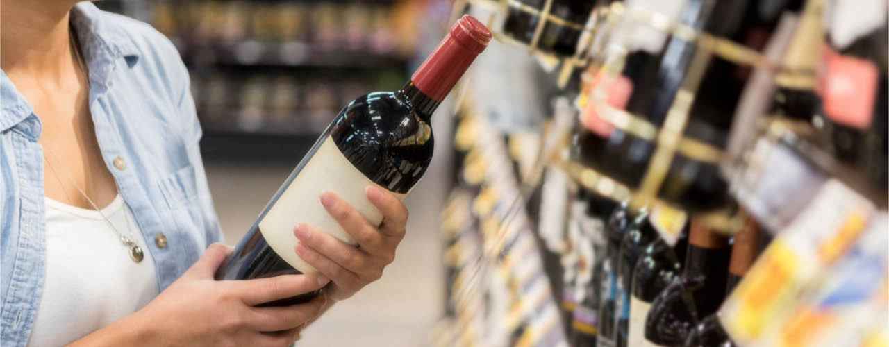 Frau hält im Supermarkt eine Weinflasche vor sich in der Hand und liest das Etikett