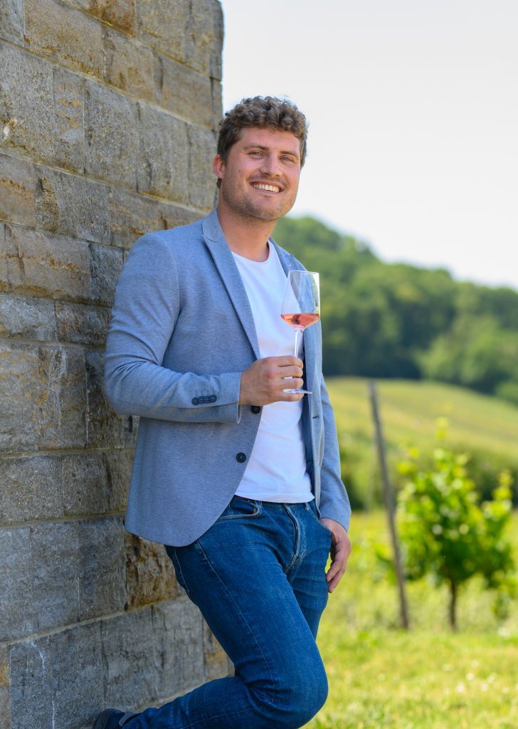 Daniel Drautz lehnt mit einem Glas Wein der Genossenschaftskellerei Heilbronn an einer Wand