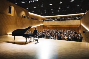 Die Tauberphilharmonie von innen, Blick von der Bühne in den mit Menschen gefüllten Saal.